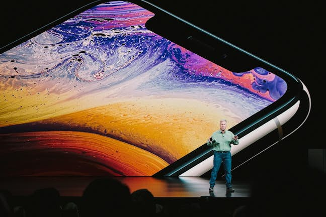 man speaking on stage with image of phone behind him