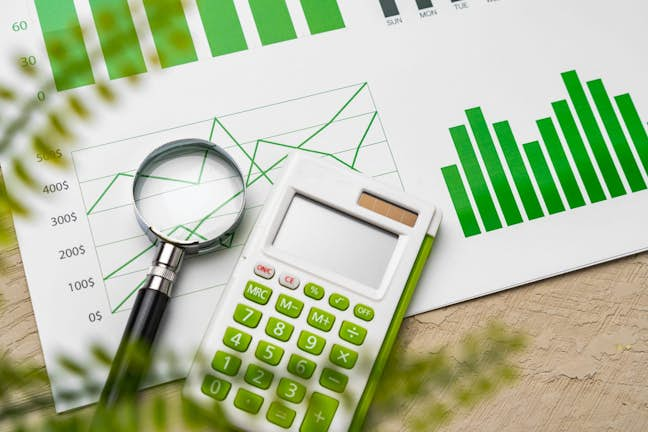 pieces of paper with green charts, magnifying glass and calculator