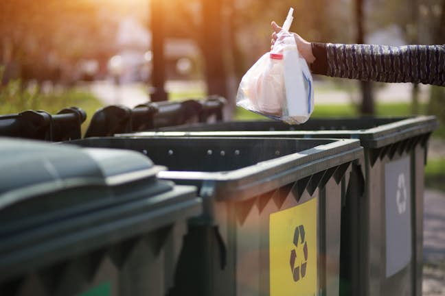 an arm reaching out to put something in the recycling bin