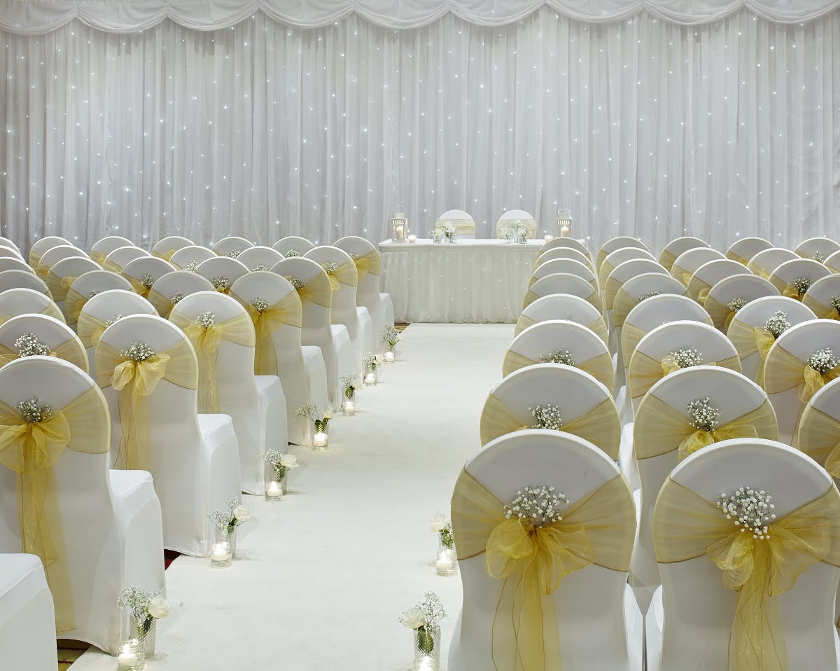 Wedding ceremony setup in Thomas Ambler Suite, Leeds Marriott, with white chairs and floral decor.