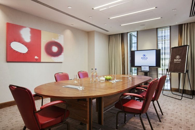 Modern meeting room with round table and red chairs at Hilton Liverpool City Centre.