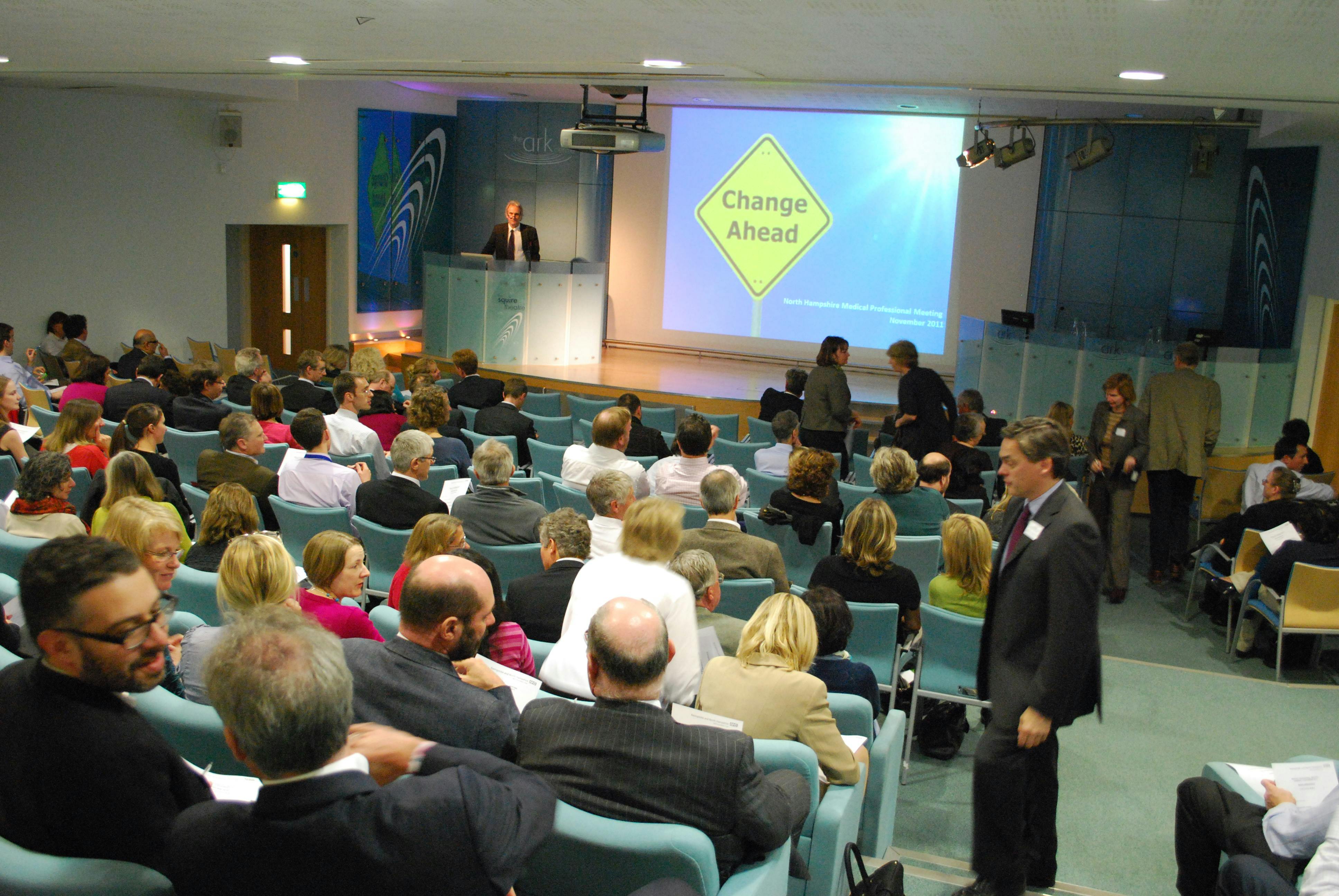 Squire Theatre conference with engaged audience and "Change Ahead" sign for innovation.