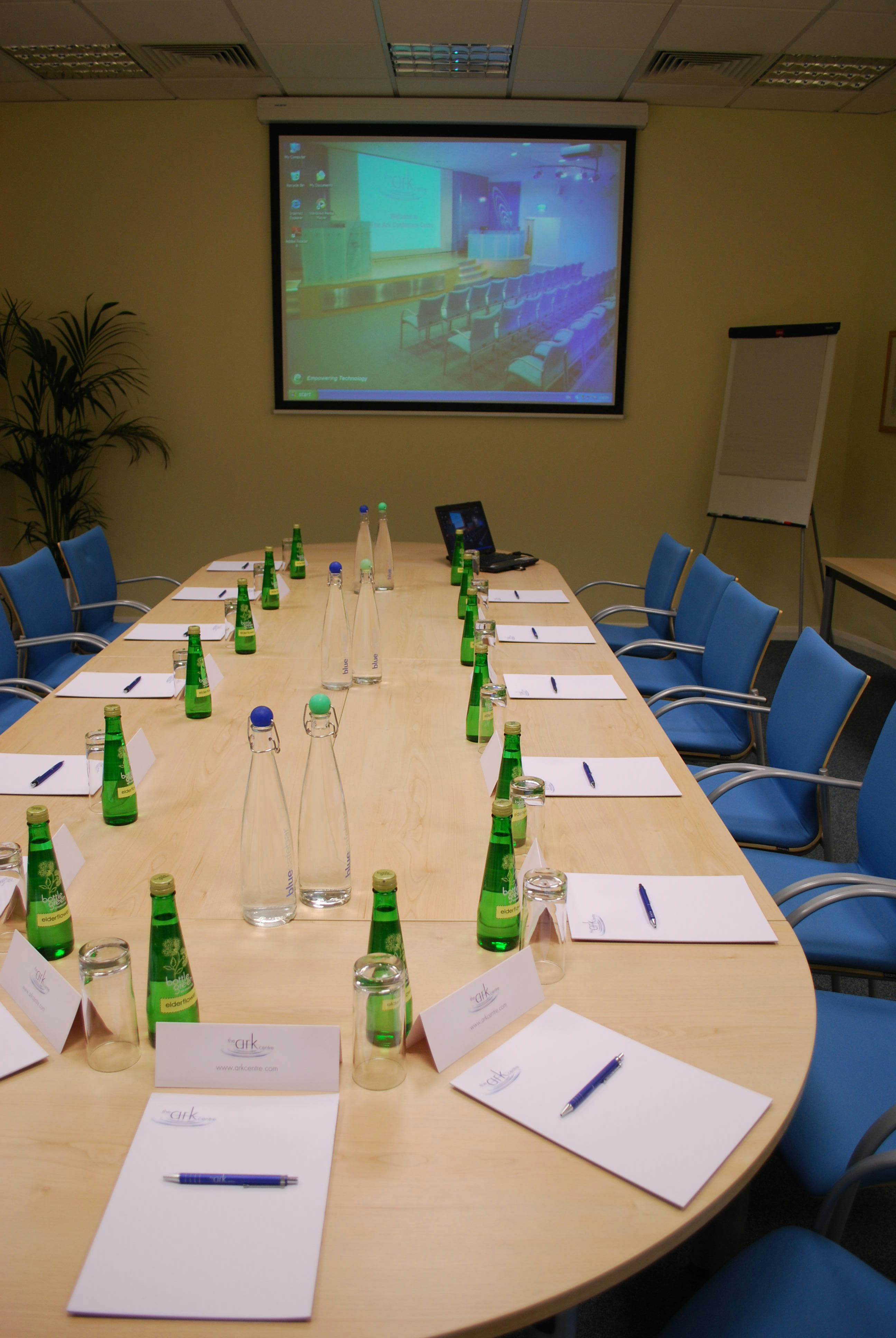 Meeting room at Ark Conference Centre with long table, notepads, and projector for events.