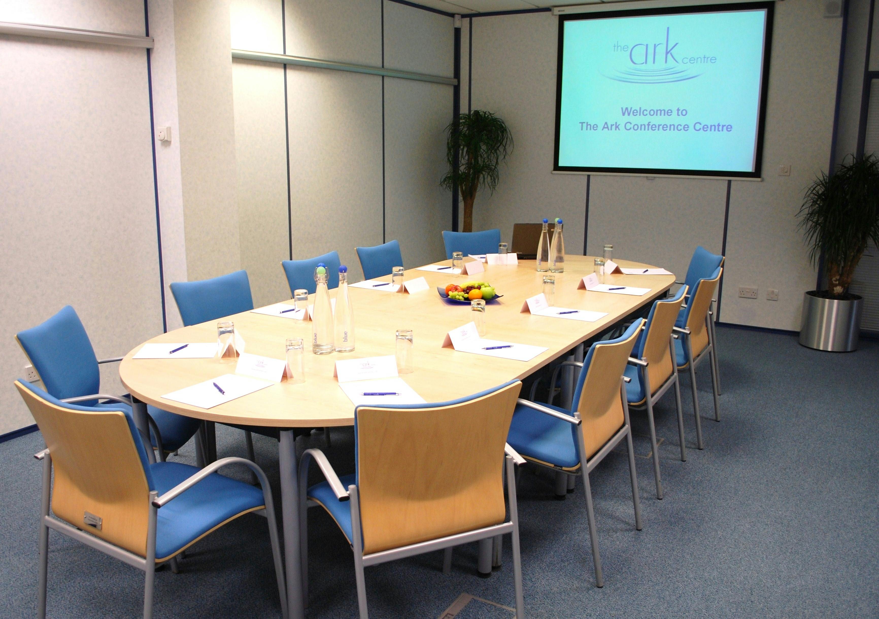 Conference room at The Ark Centre with oval table, blue chairs, and branding screen.