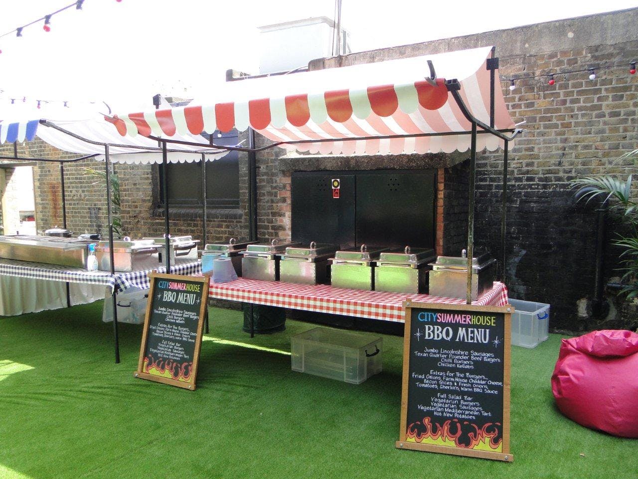 Summer party catering setup with striped tents and BBQ menu in outdoor venue.