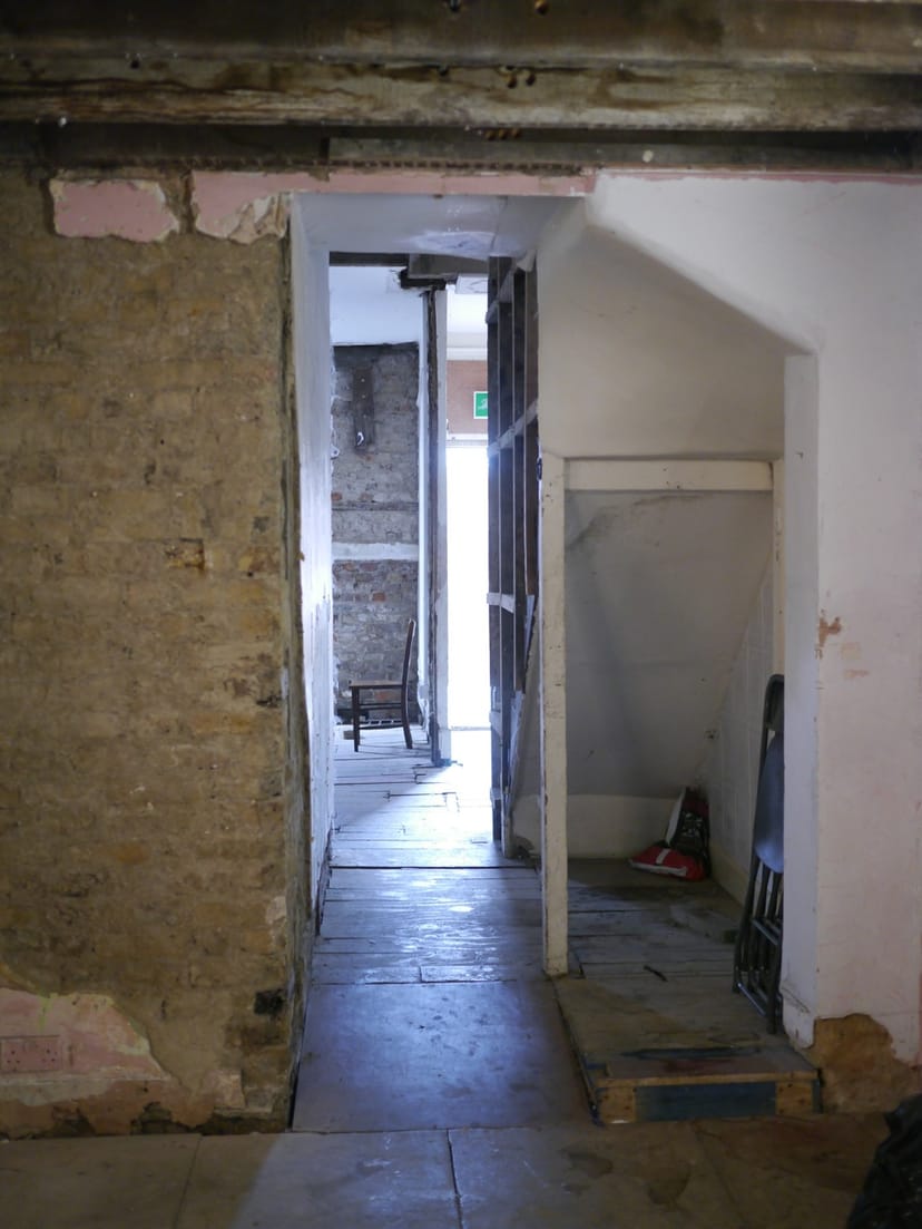 Narrow corridor with rustic walls leading to bright exit, perfect for events and branding.