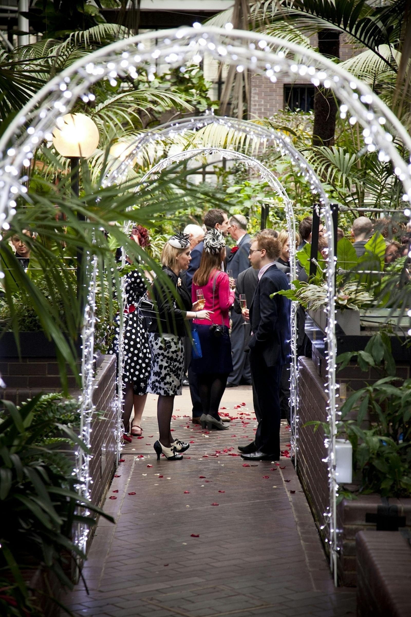 Networking event in The Conservatory, Barbican Centre, with elegant archway and tropical decor.
