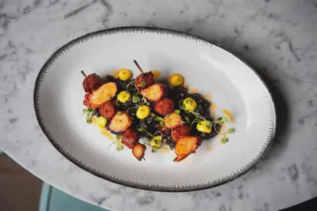 Skewered seafood on black lentils, perfect for upscale event catering.