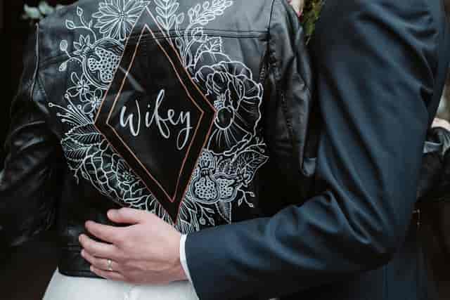 Stylish couple at wedding in The Music Club Room, bride in floral-embroidered leather jacket.
