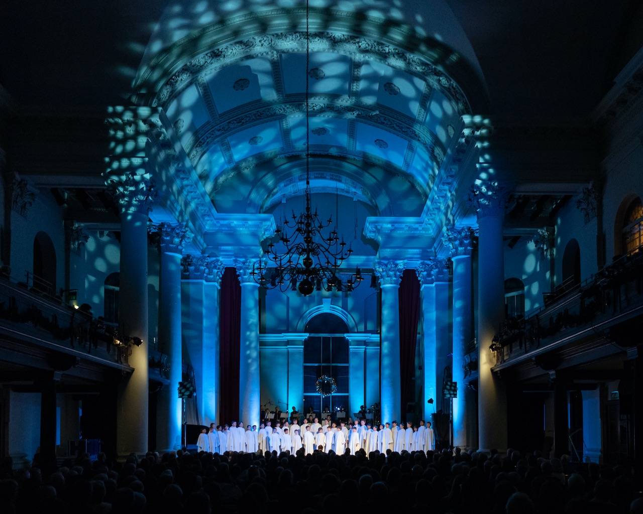 Choir performance in Sinfonia Smith Square with dramatic blue lighting and elegant architecture. - Banner