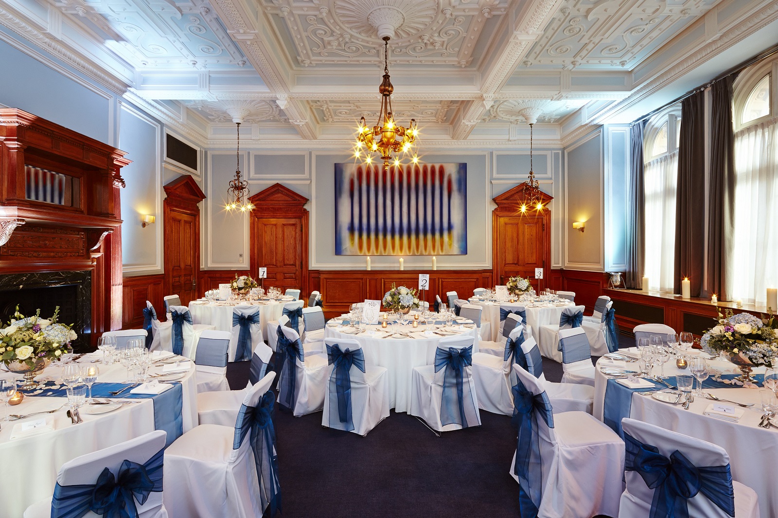 Elegant banquet room at Andaz London, featuring round tables with white linens and blue sashes.