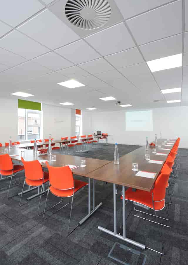 Buzz studio meeting room with U-shaped tables and bright orange chairs for events.
