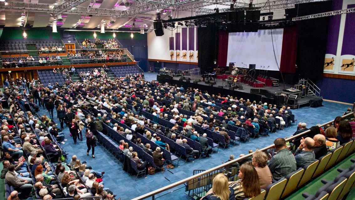 Centaur auditorium at Cheltenham Racecourse, filled audience for a live event.