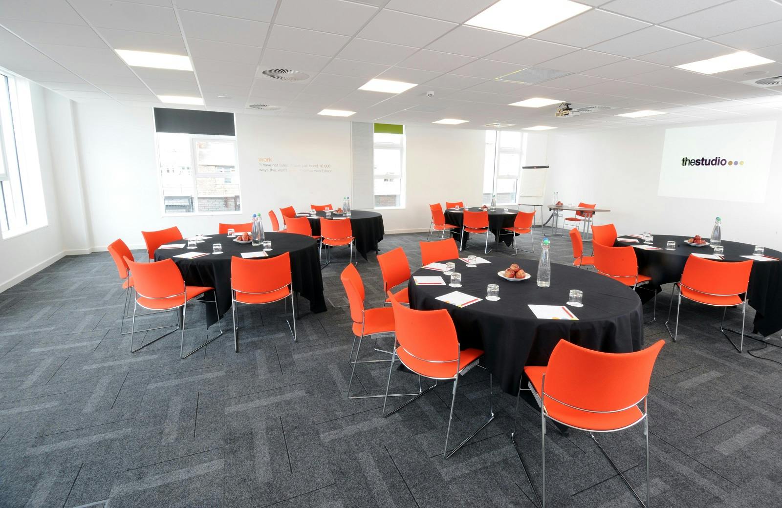 "Modern meeting space in Manchester with round tables and vibrant orange chairs for workshops."