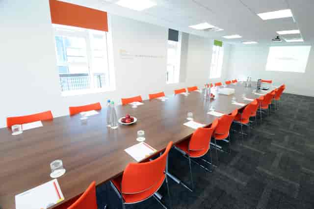 Modern conference room in Manchester with wooden table and orange chairs for corporate meetings.