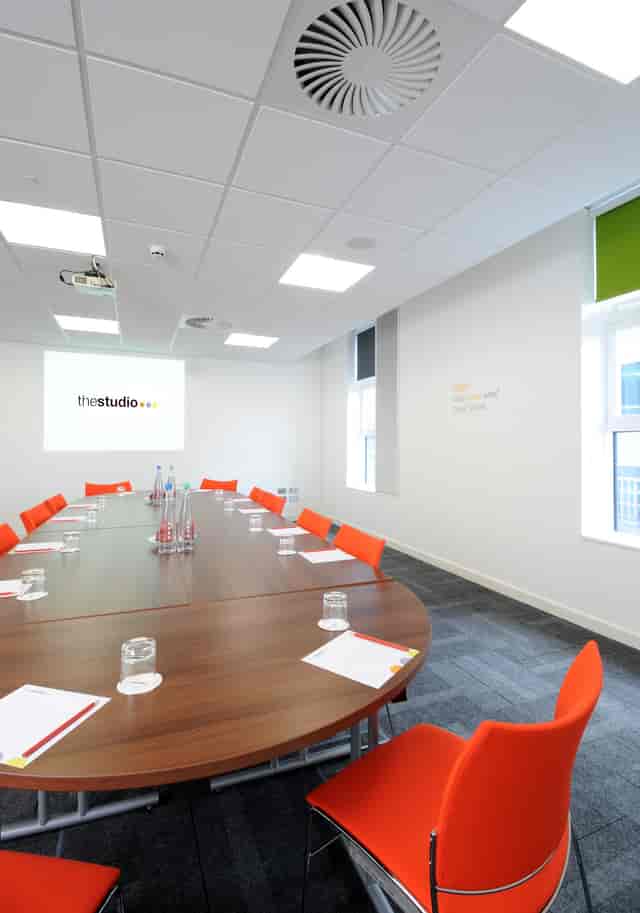 Modern meeting room in Manchester with wooden table and orange chairs for corporate workshops.