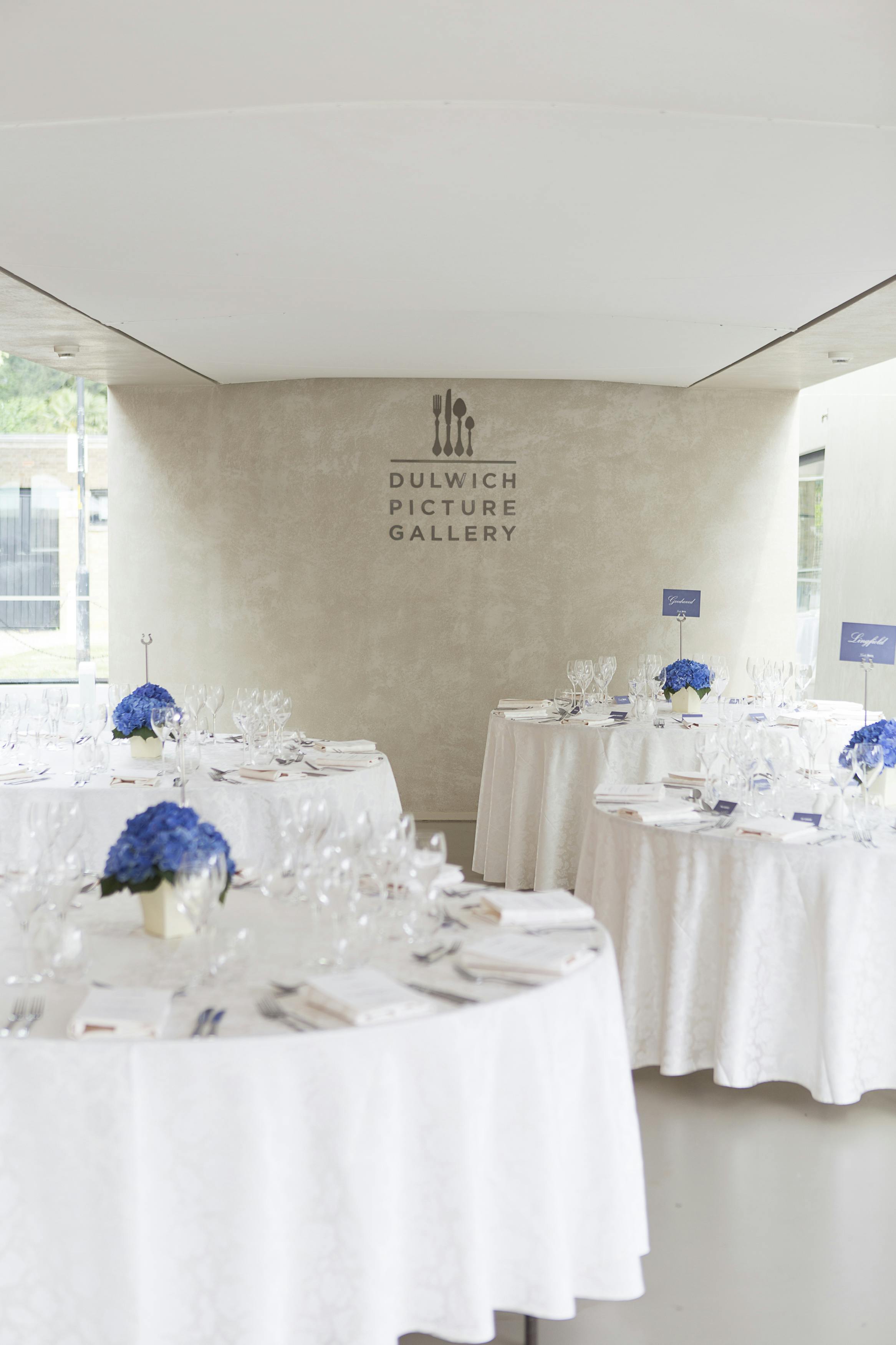 Elegant event space at Dulwich Picture Gallery with blue floral centerpieces.