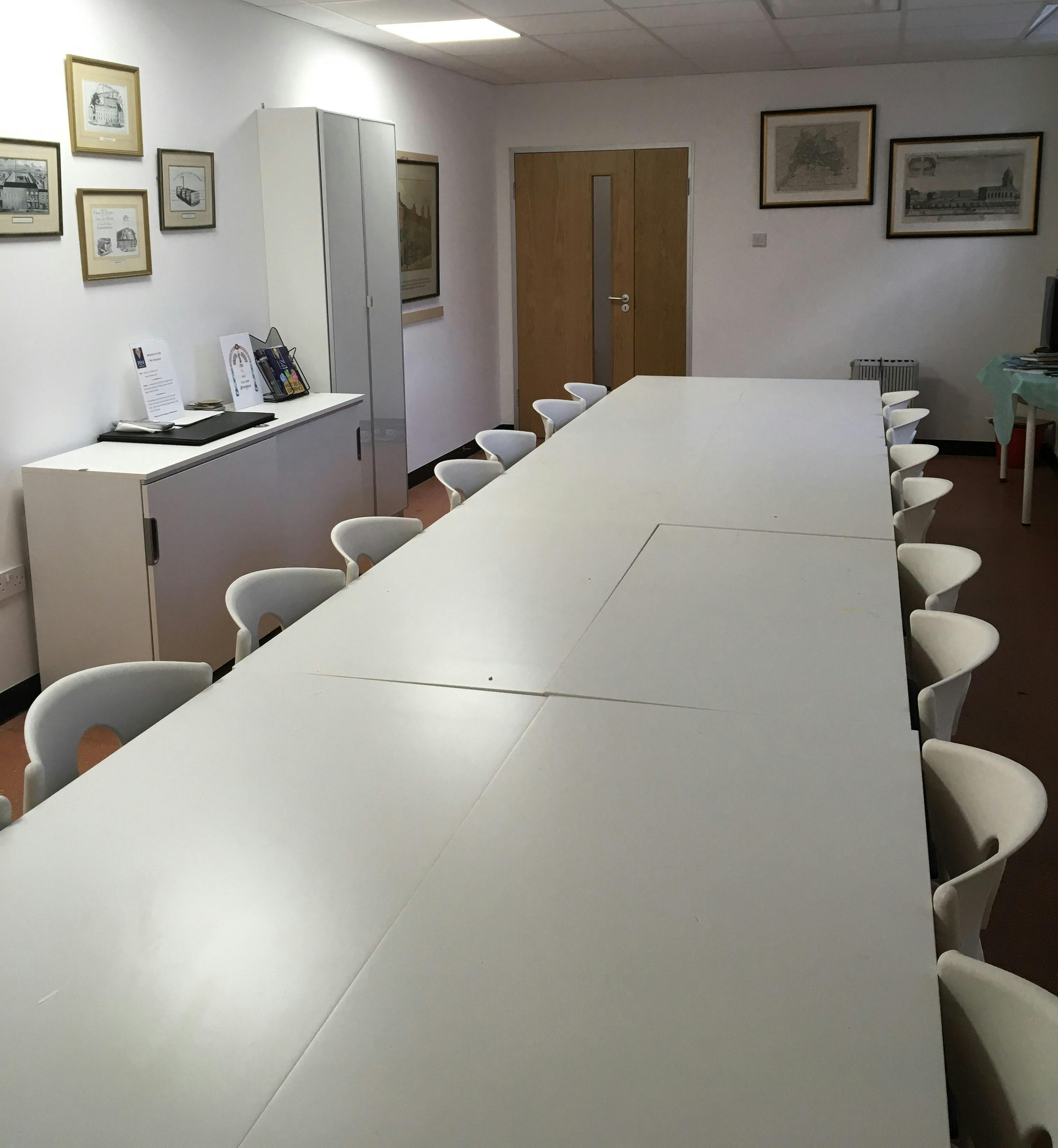 Minimalist meeting room at Pen Museum with white table and chairs, perfect for events.
