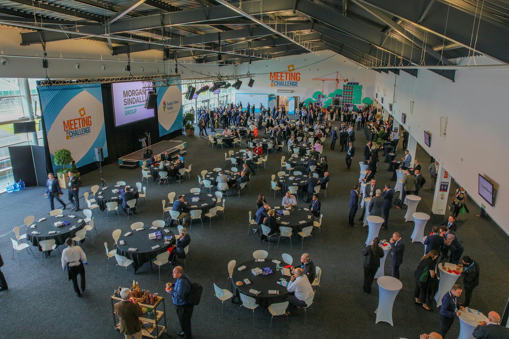 "Hall 3 at Silverstone Centre: bustling networking event with round tables and screens."