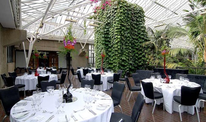 Elegant event space at Barbican Centre with round tables and lush greenery.