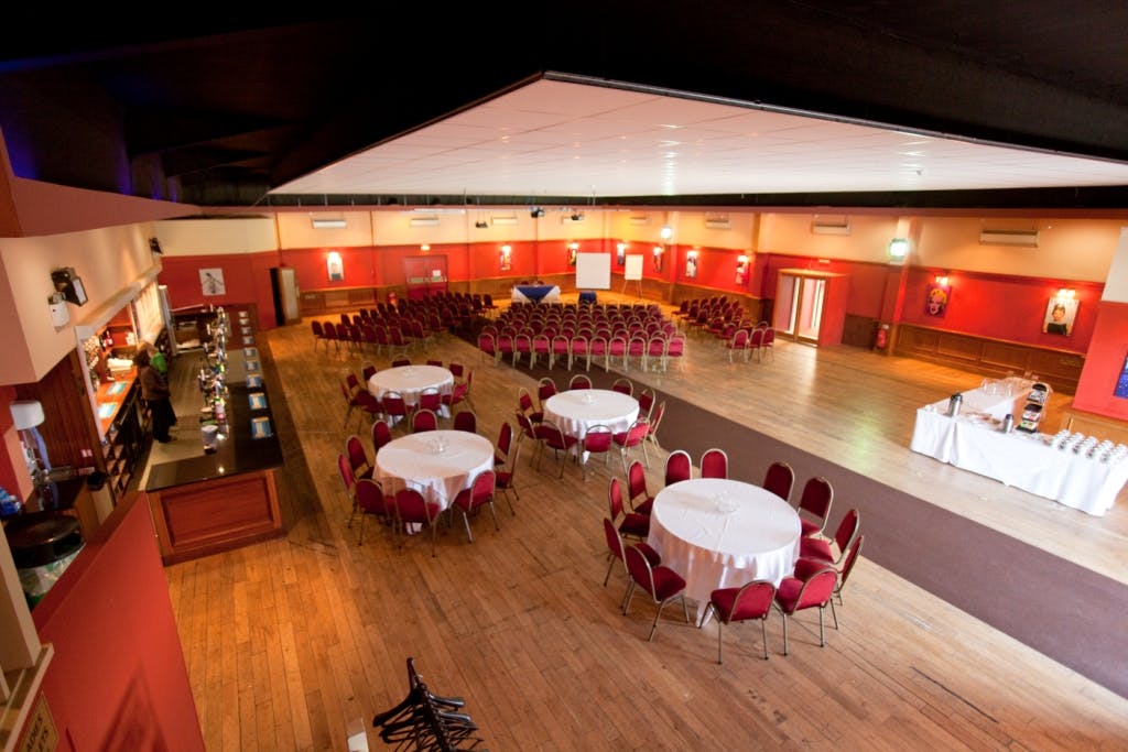 Spacious event venue at The Dray, featuring round tables and red chairs for meetings.