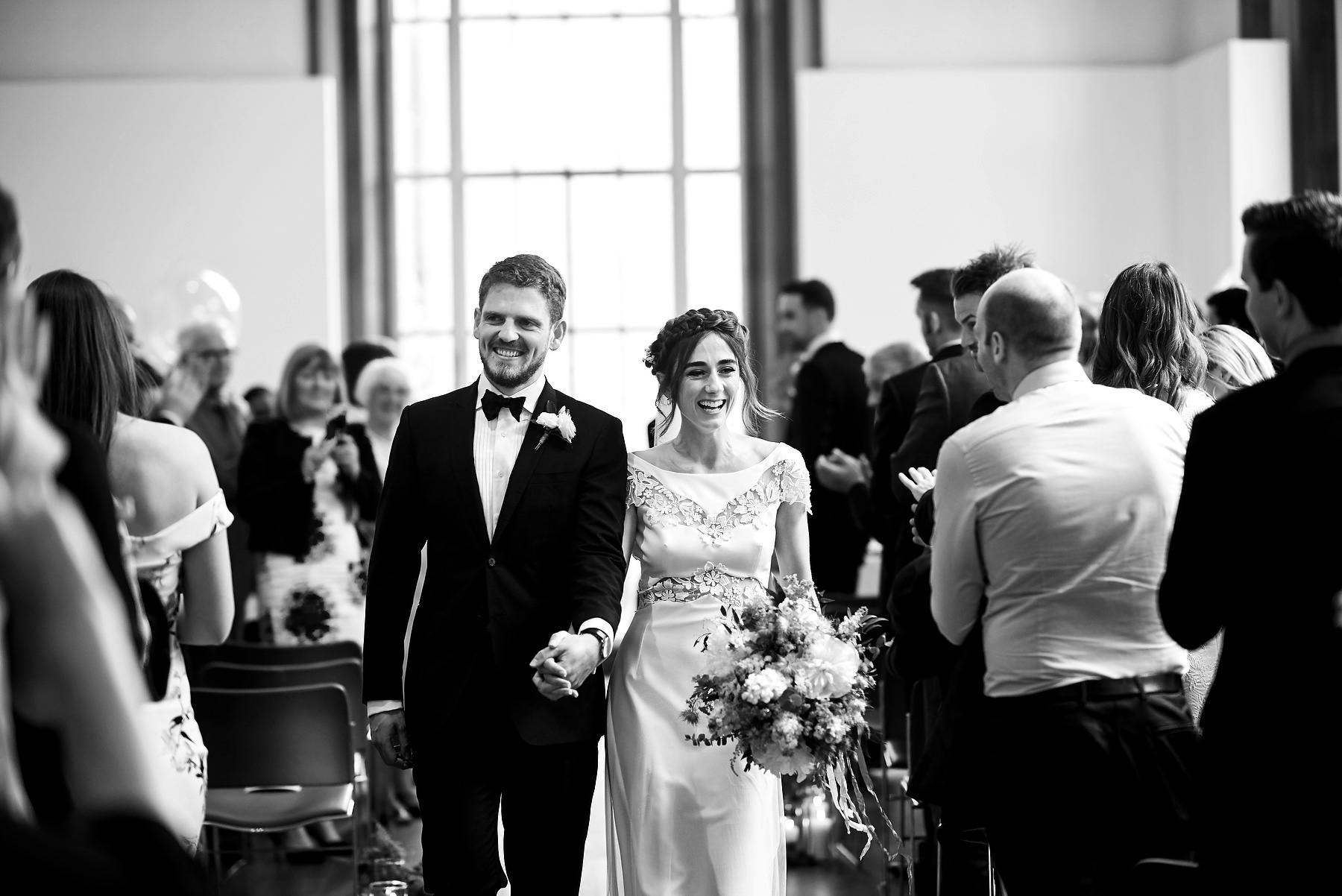 Joyful couple walking down the aisle at a wedding in RIBA Gallery, London.