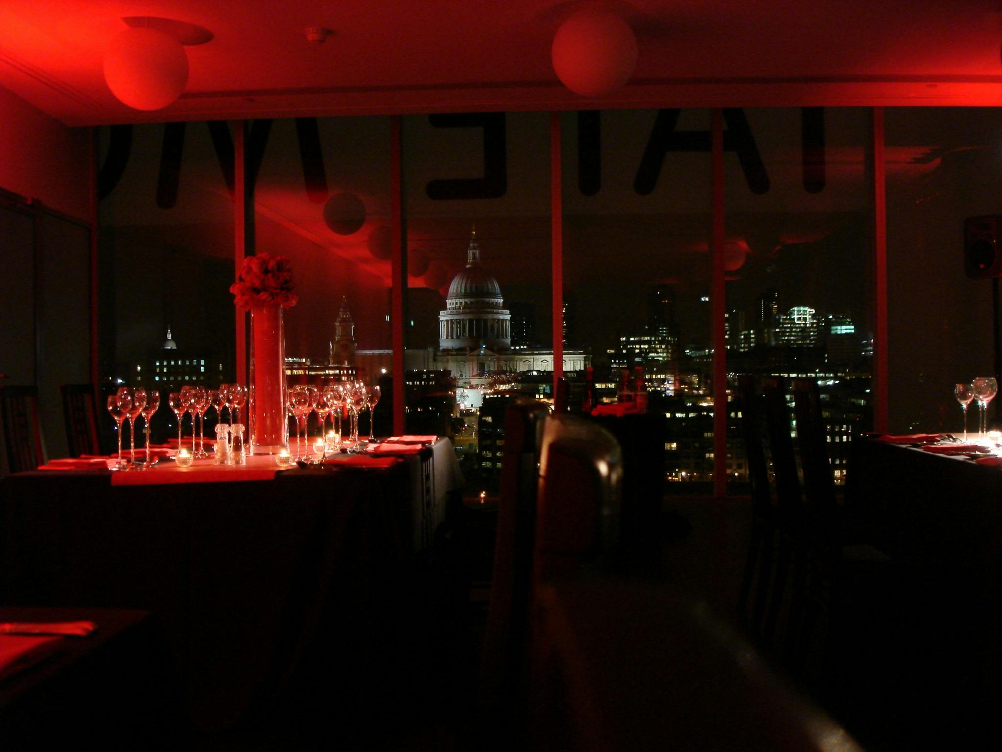 Elegant dinner setup in Tate Modern's East Room with red lighting and St. Paul's Cathedral view.