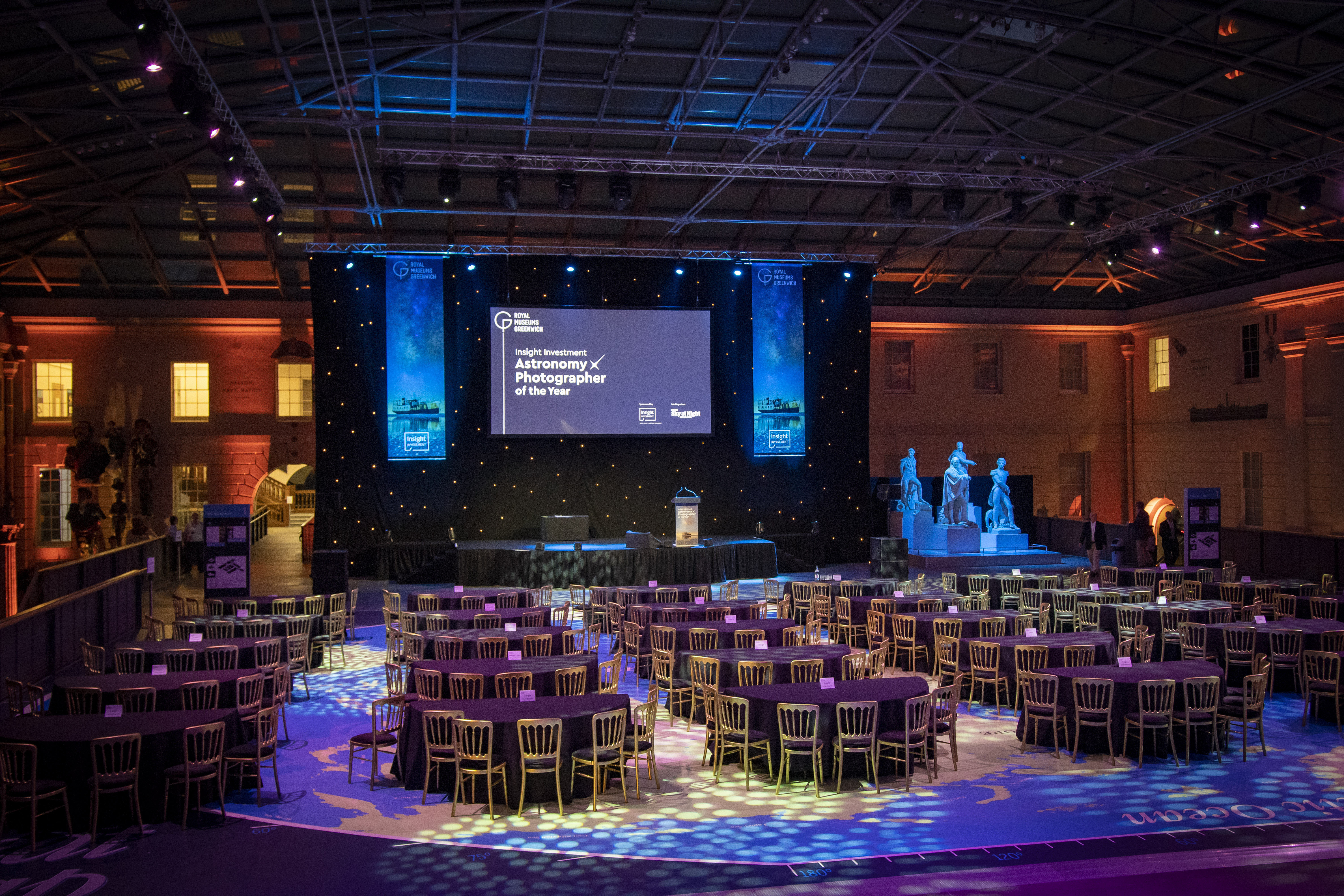Elegant event space at National Maritime Museum with round tables and dynamic stage lighting. - Banner