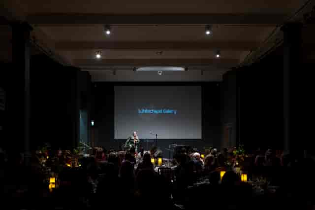 "Elegant event in Whitechapel Gallery with engaged audience and candlelit tables."