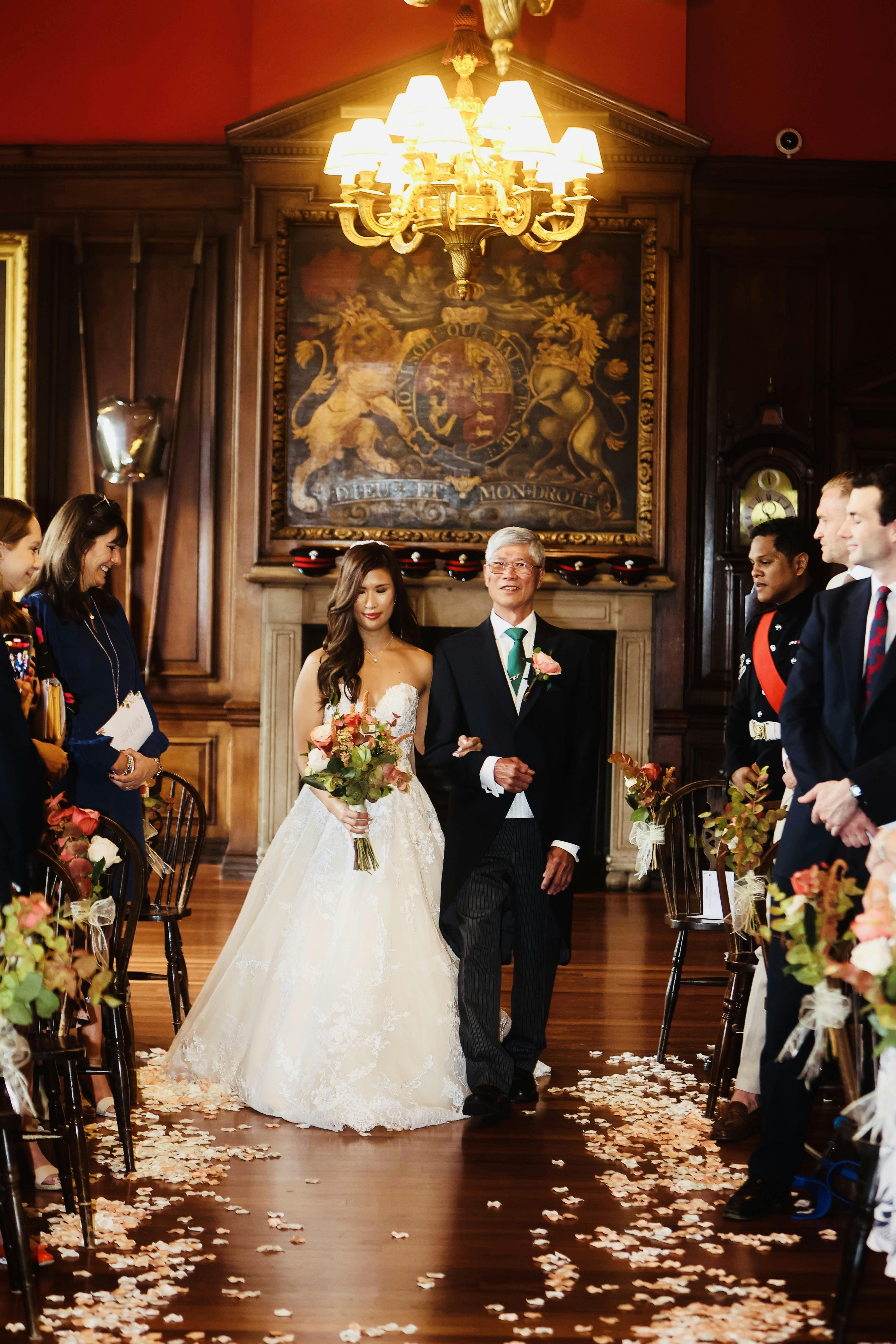 Wedding ceremony in The Long Room, bride and father at altar, elegant floral arrangements.