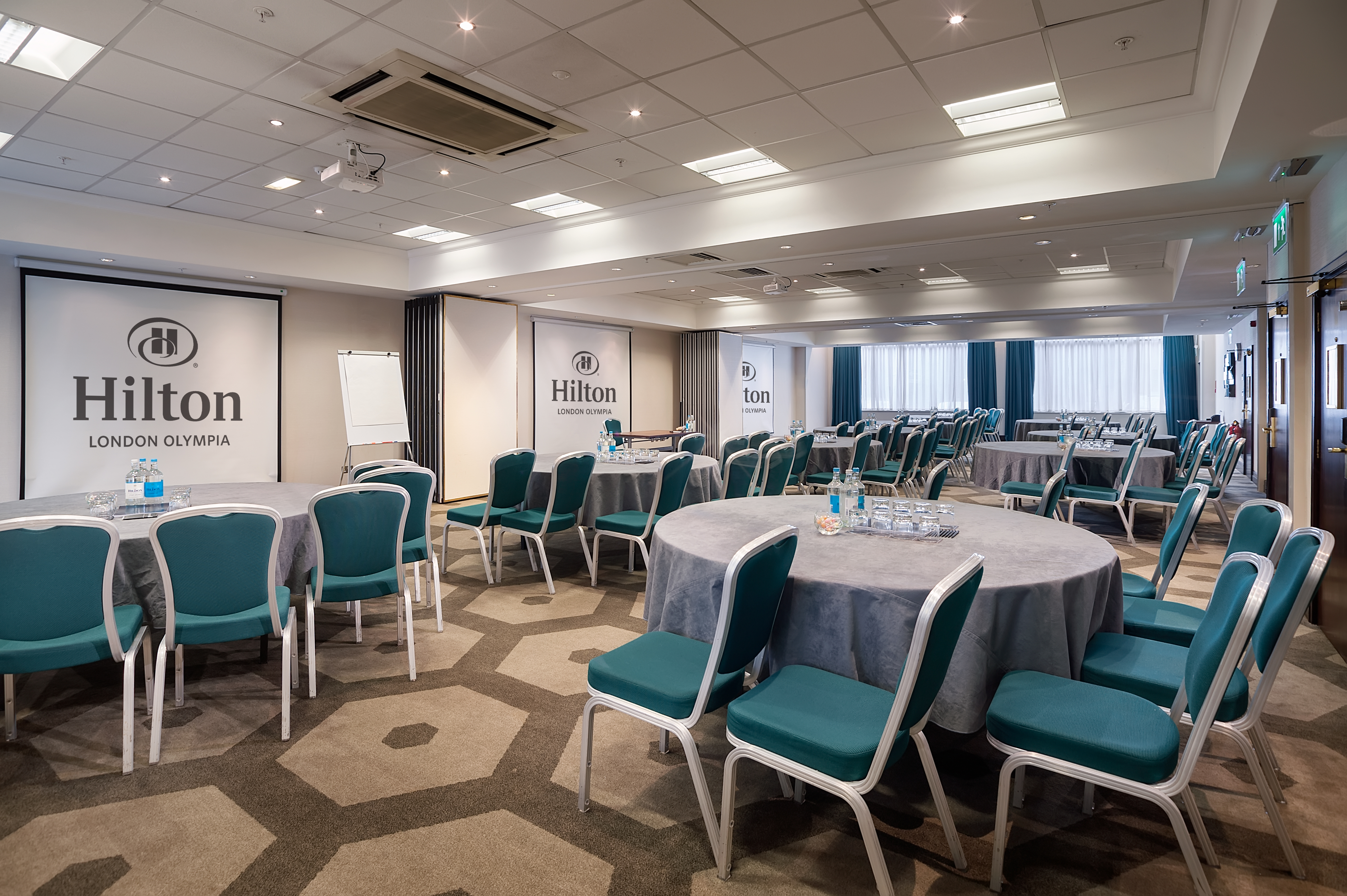 Pembroke Suite at Hilton London Olympia, featuring round tables and teal chairs for corporate events. - Banner