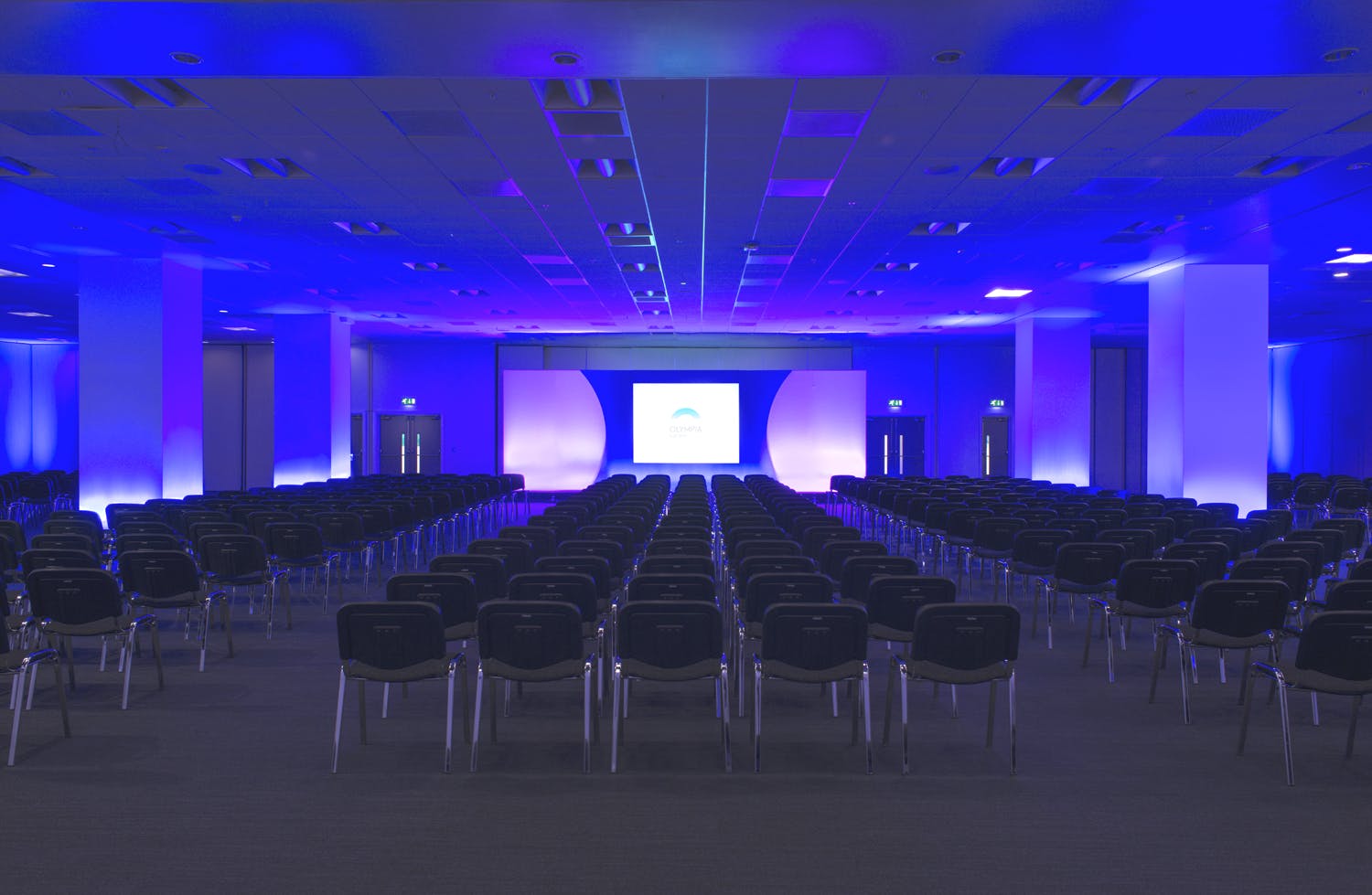 East Hall in Olympia London, spacious conference venue with blue lighting and black chairs.