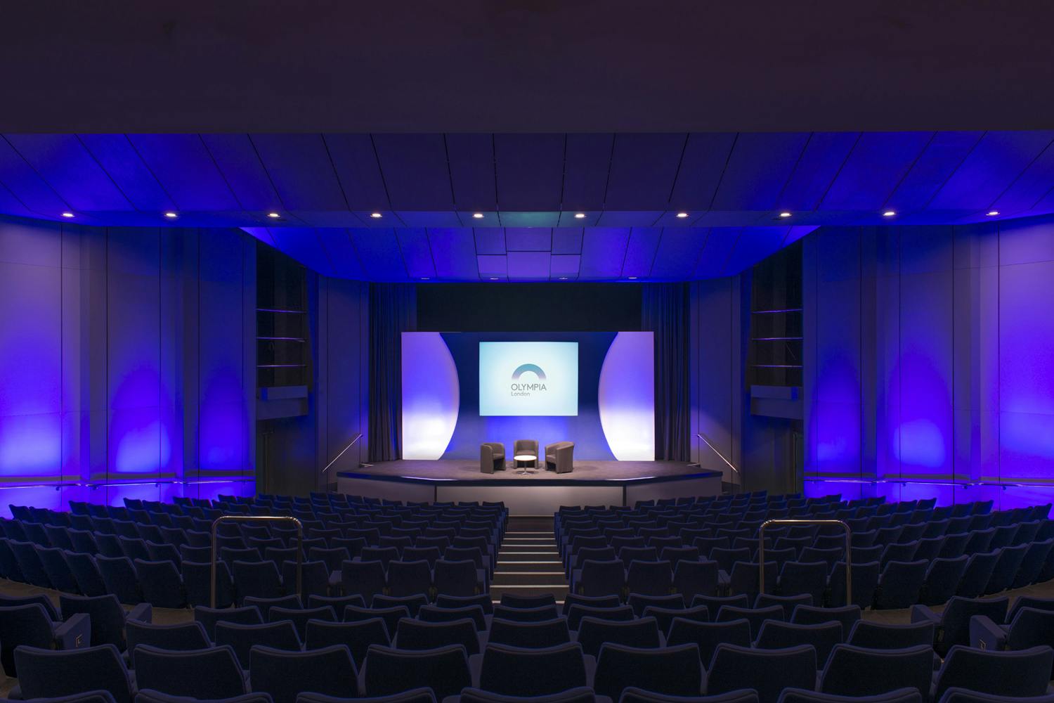 Auditorium in Olympia London with stage, blue lighting for presentations and events.