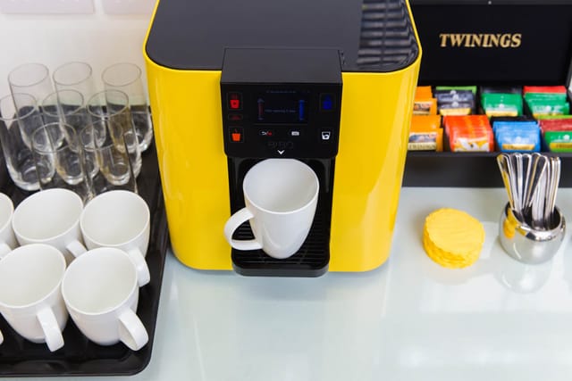 Vibrant coffee station with yellow machine in BakerStreetQ Meeting Space for events.