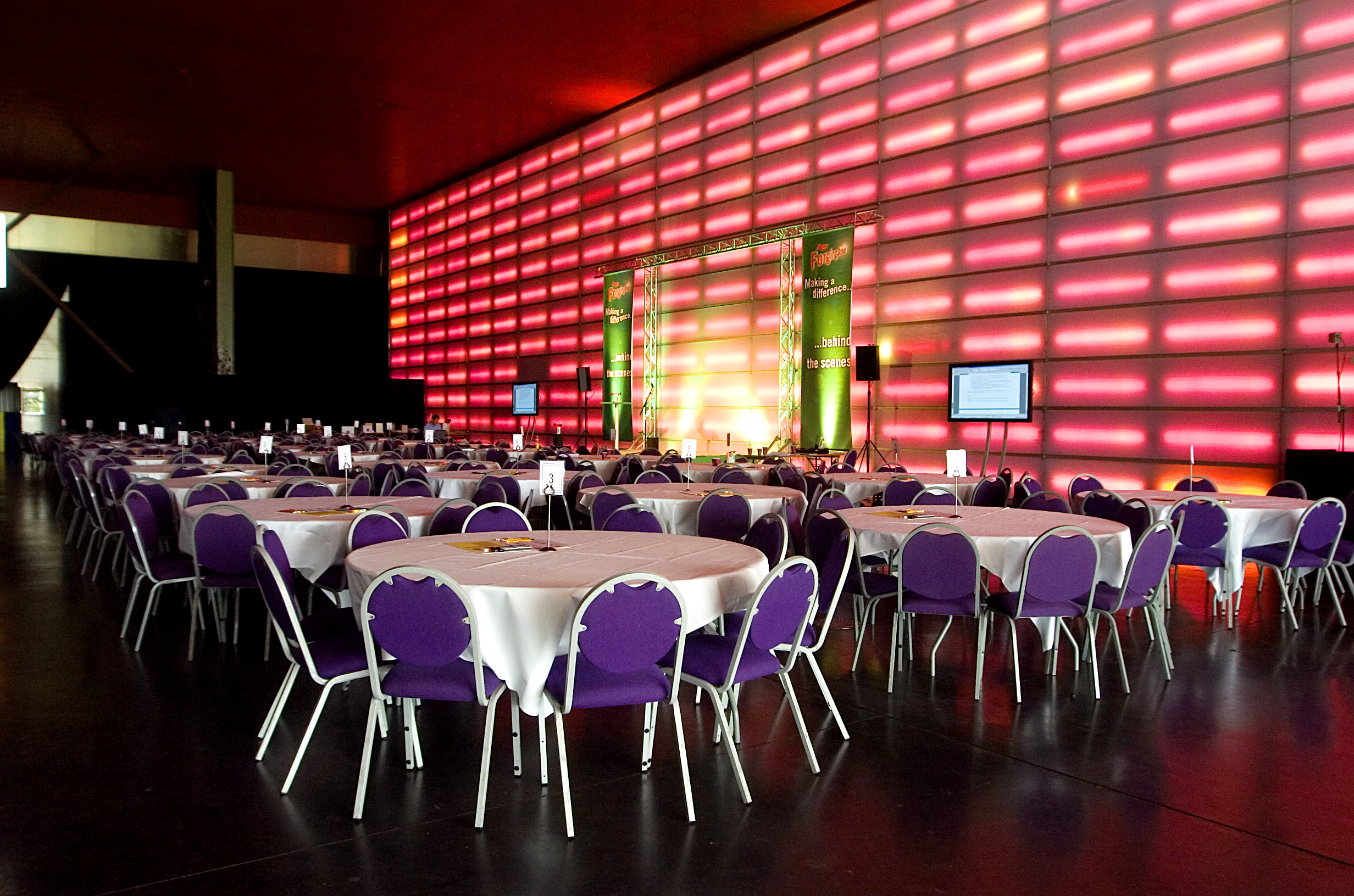 The Red Hall at MAGNA: vibrant event space with round tables and purple chairs. - Banner