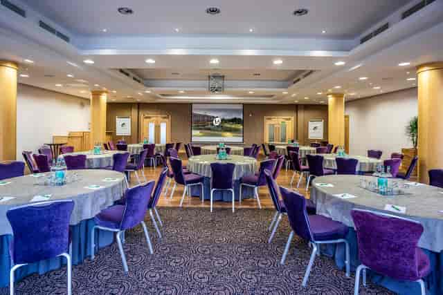 Wimbledon Room at The Lensbury: elegant event space with gray tables and purple chairs.