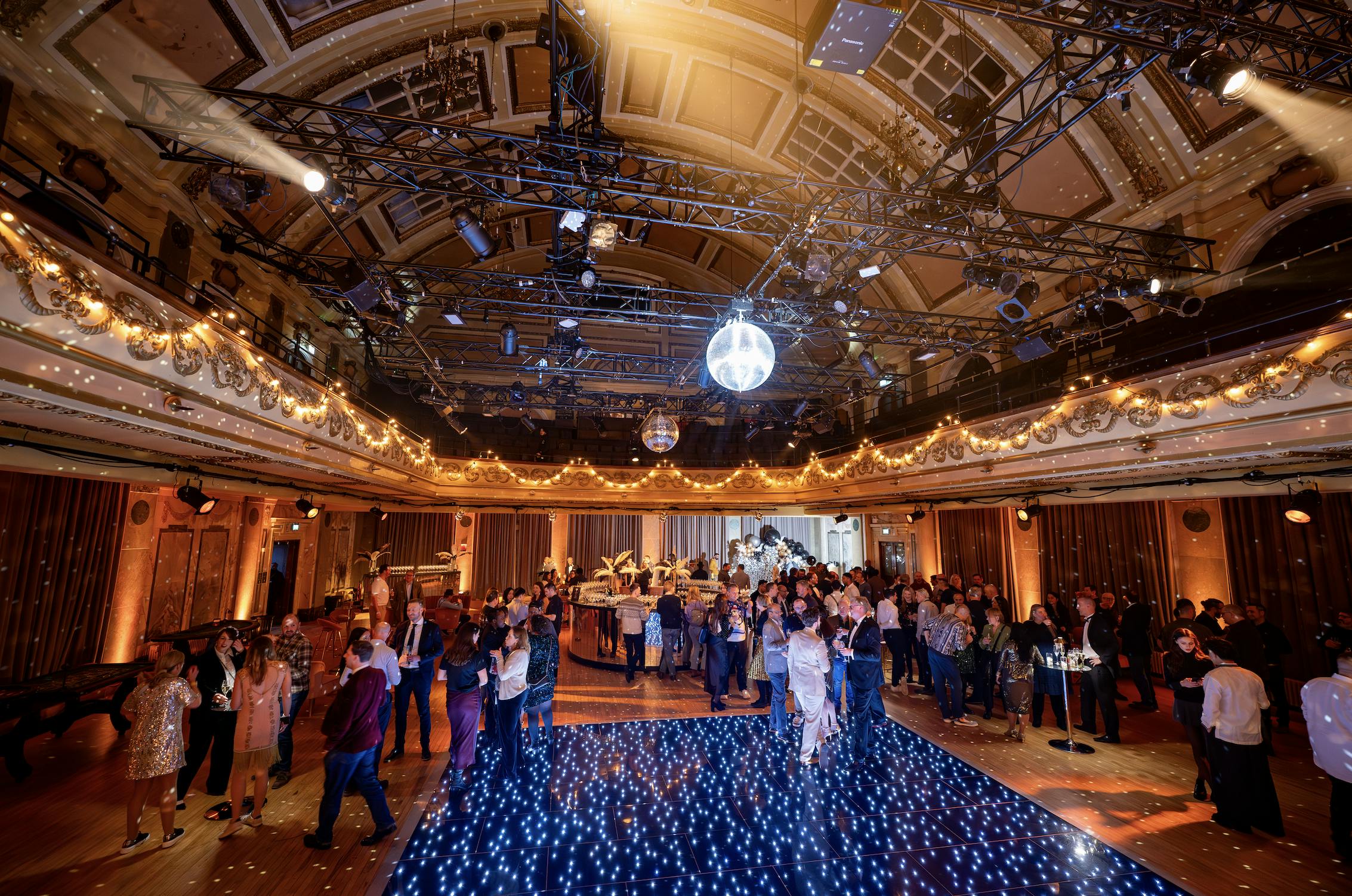 Elegant Christmas gala with string lights and disco ball in festive event space.