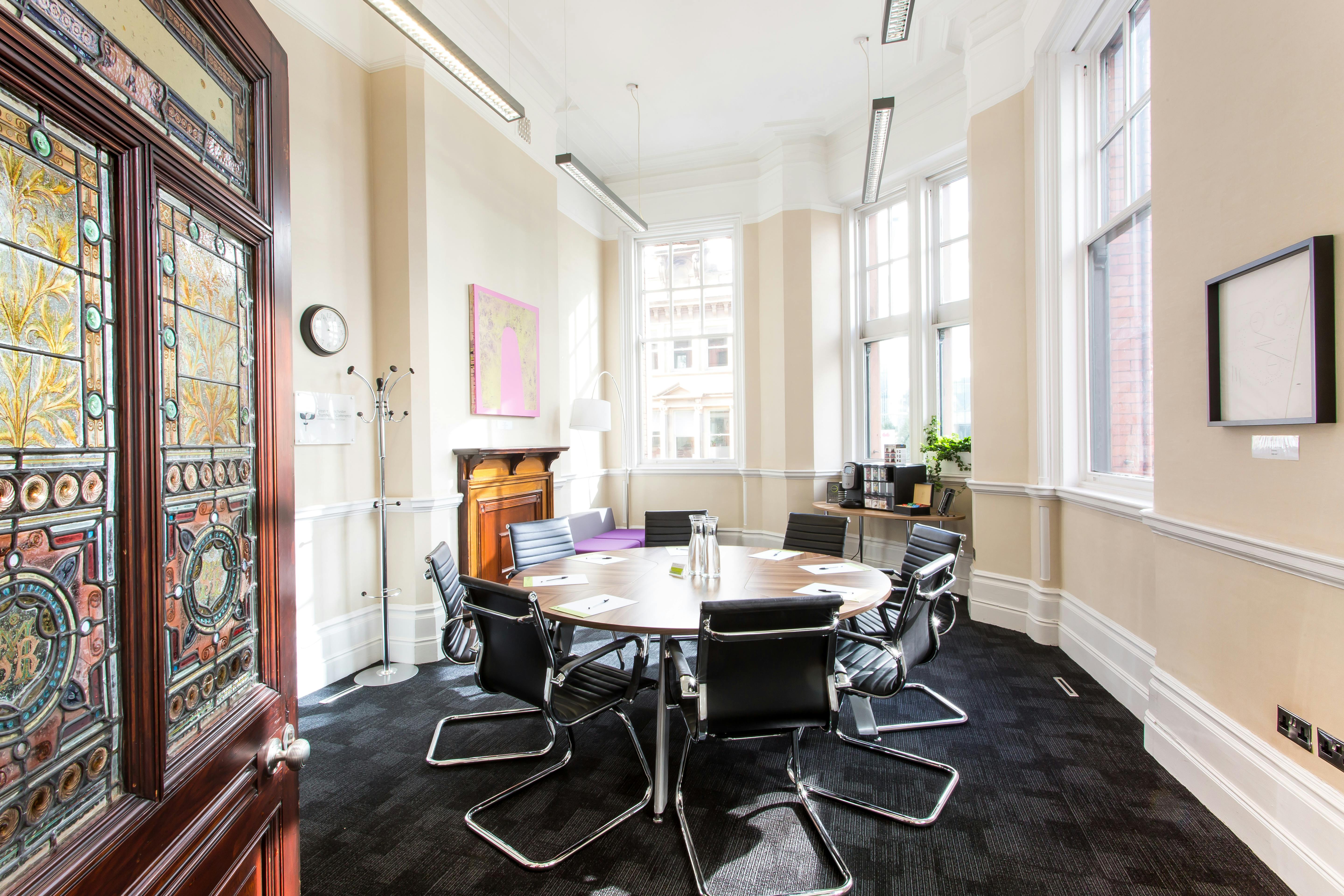 Well-lit meeting room with round table and black chairs, ideal for collaborative discussions.