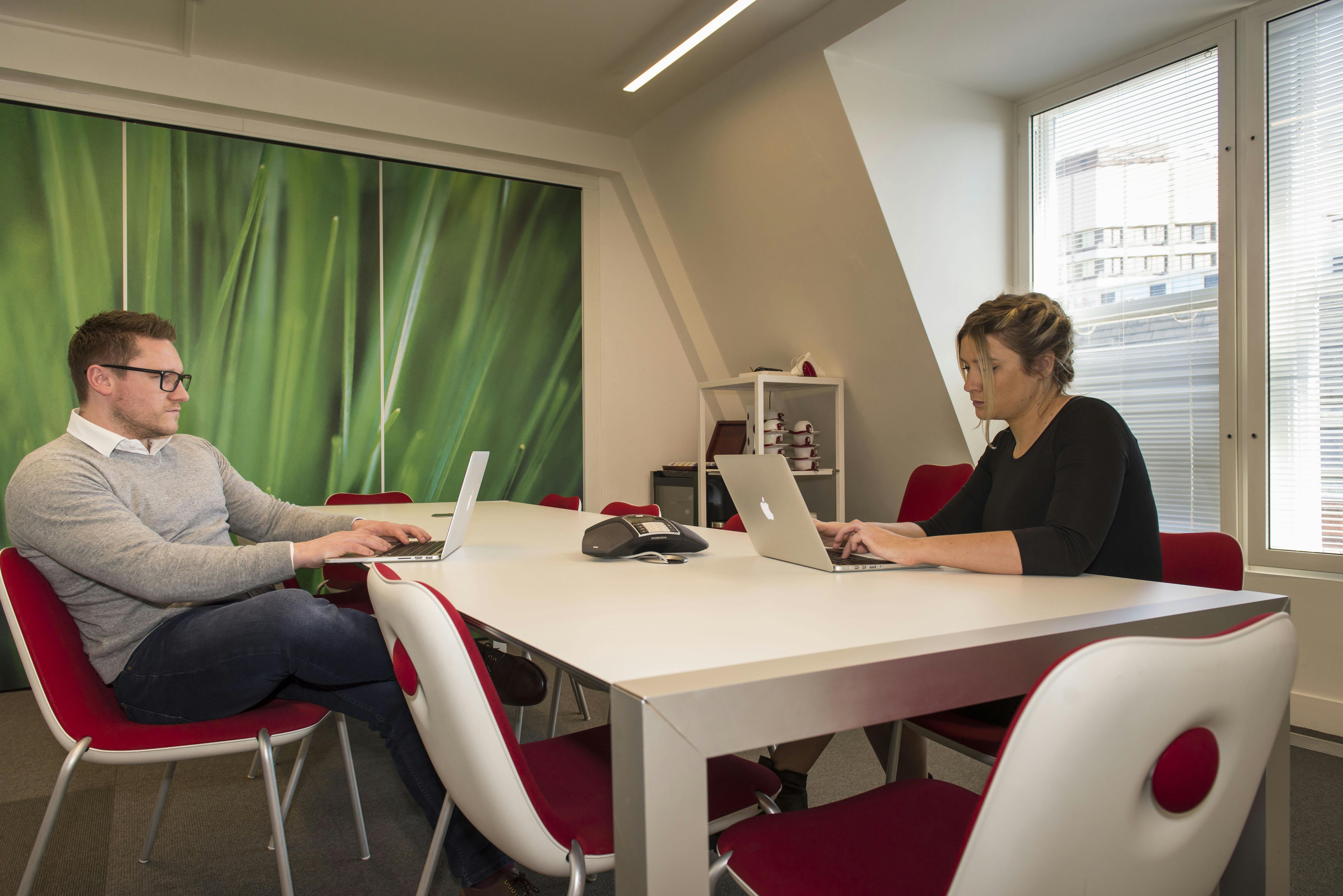 Modern meeting room e1 in eOffice - Soho, featuring professionals collaborating on laptops.