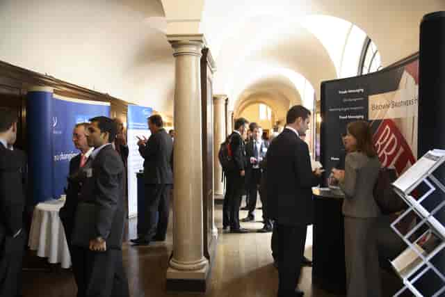 Networking event at The Cloisters, Merchant Taylors' Hall with elegant arches and exhibitor booths.