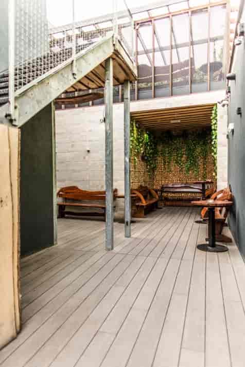 Stylish semi-outdoor meeting space at The Bridge London with wooden benches and greenery.