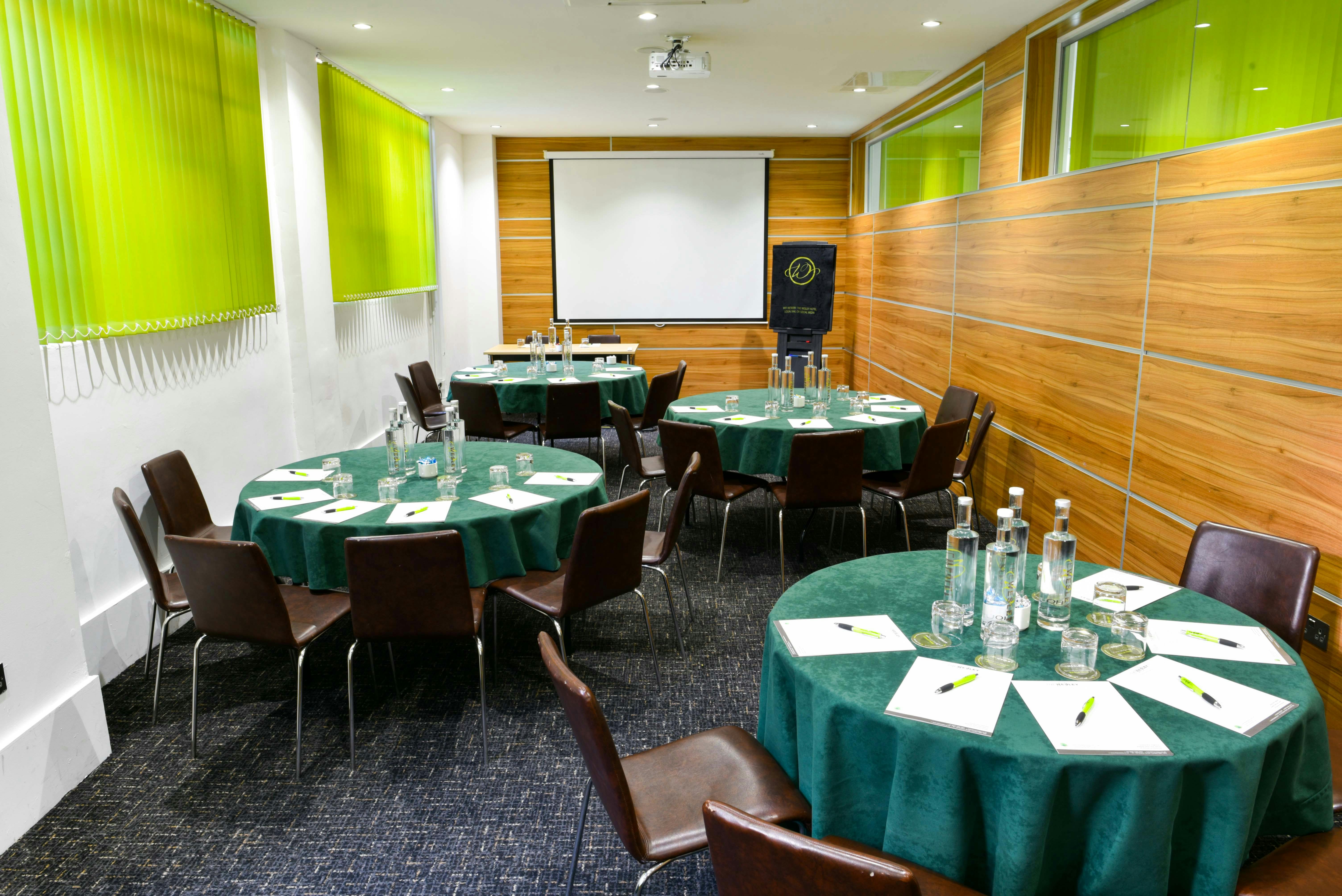 Meeting space at Wesley Euston Hotel, featuring round tables and green decor for events.