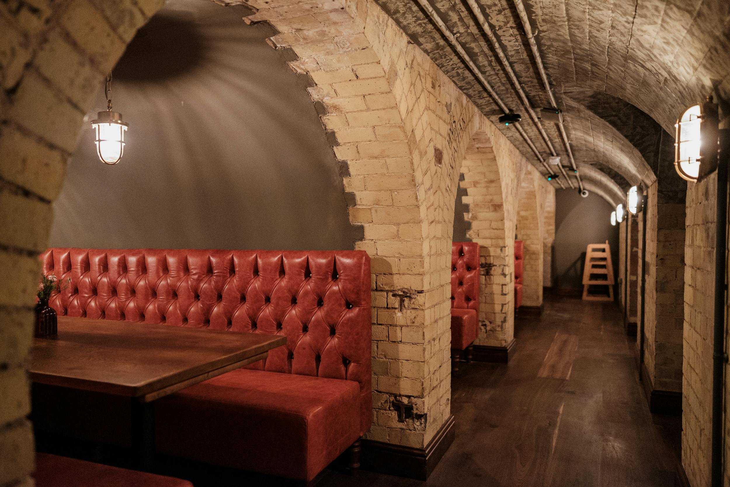 Stylish underground venue with brick arches and red leather booths for private events.