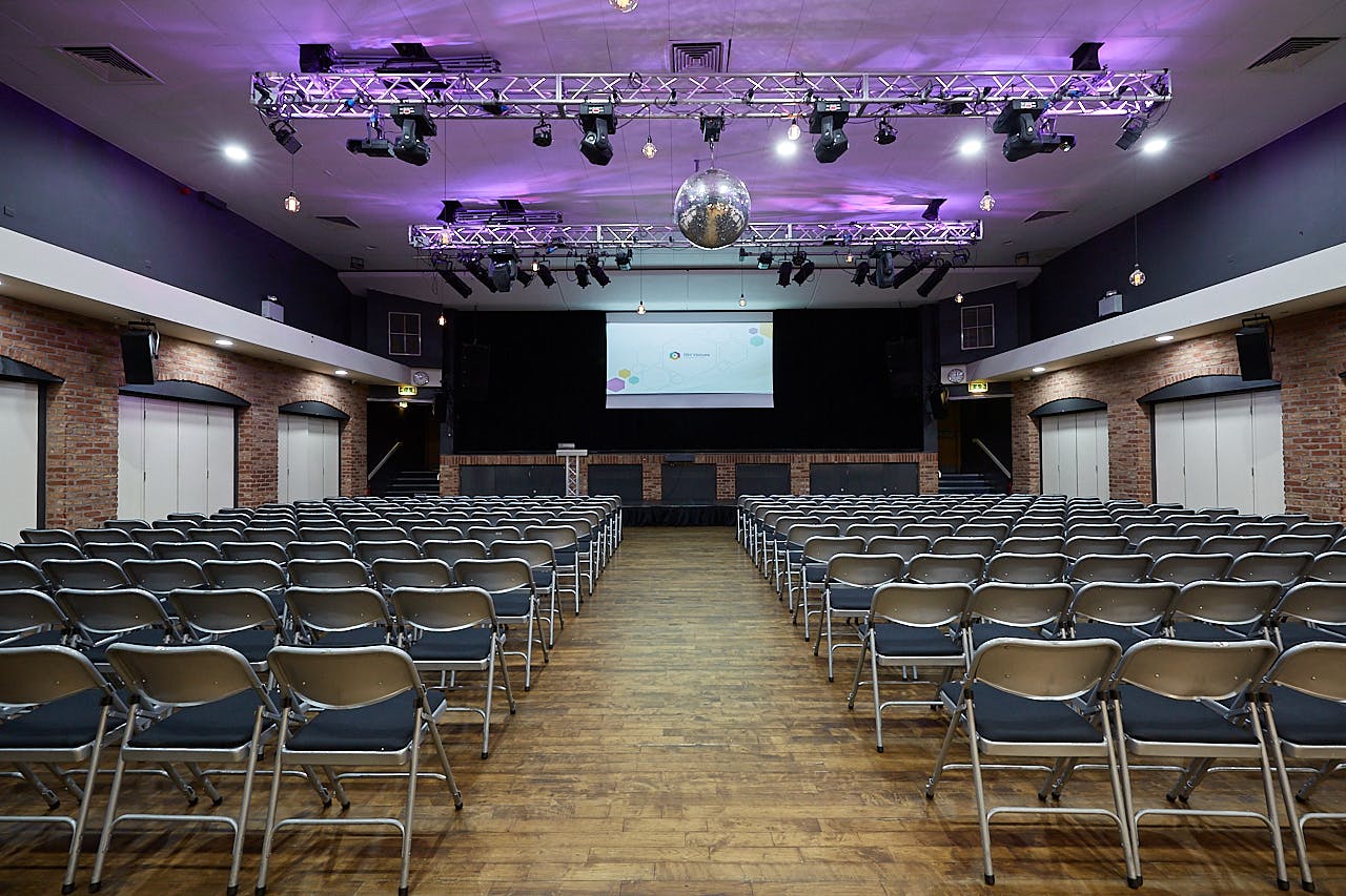 Event space with chairs and stage, purple lighting for conferences and social events.