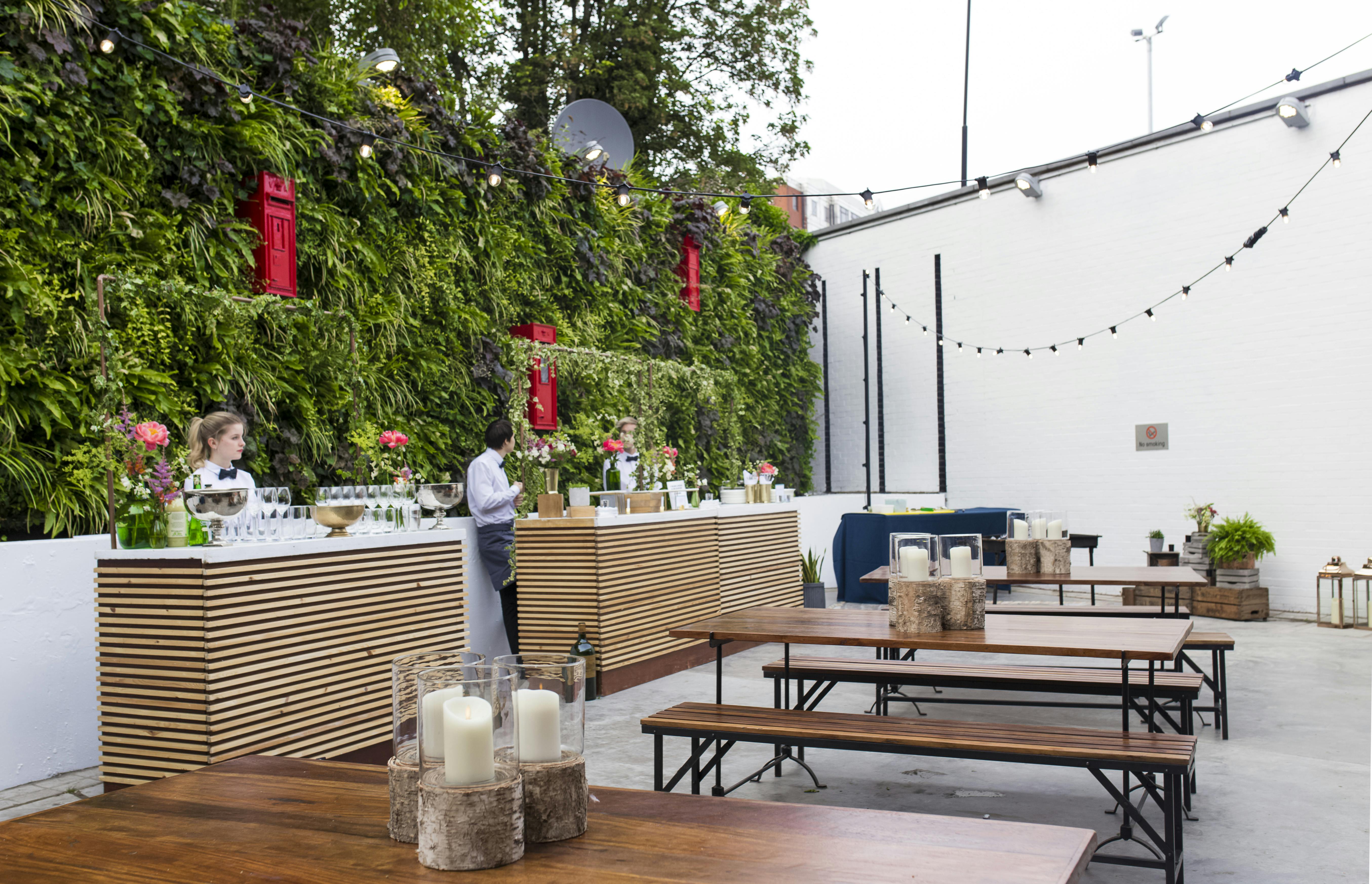 Stylish outdoor event space at The Postal Museum with lush green wall and rustic tables.