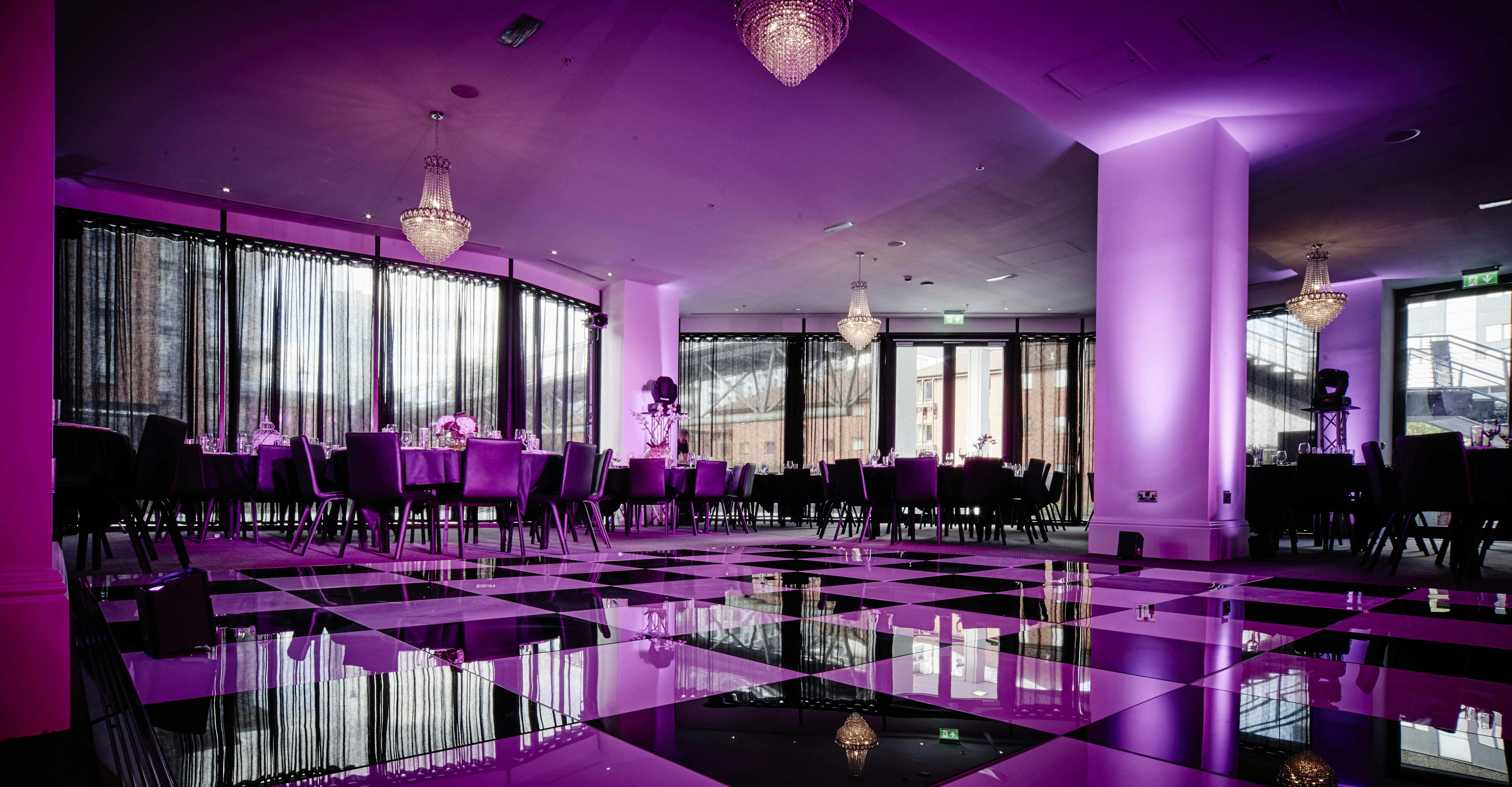 Elegant event space with checkered flooring and purple lighting, perfect for weddings or corporate events.