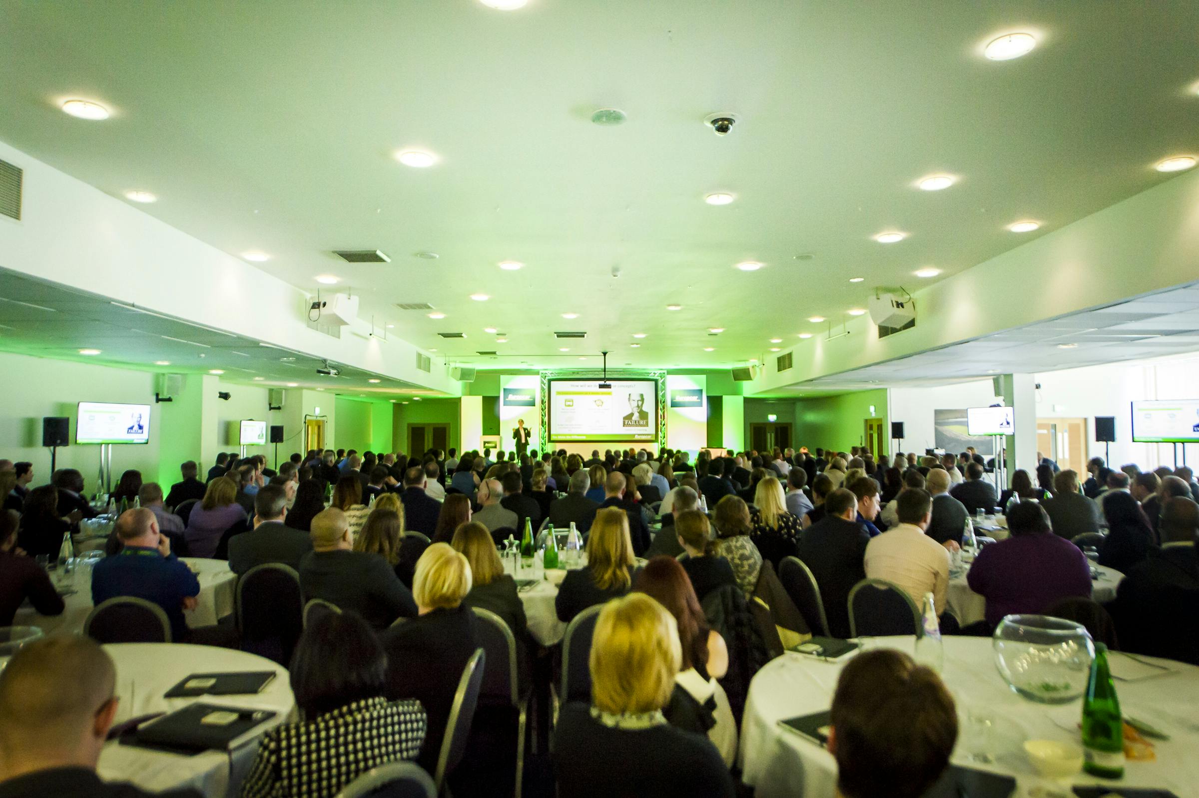 "Walkers Hall conference at Leicester City FC, bright venue with round tables and stage."