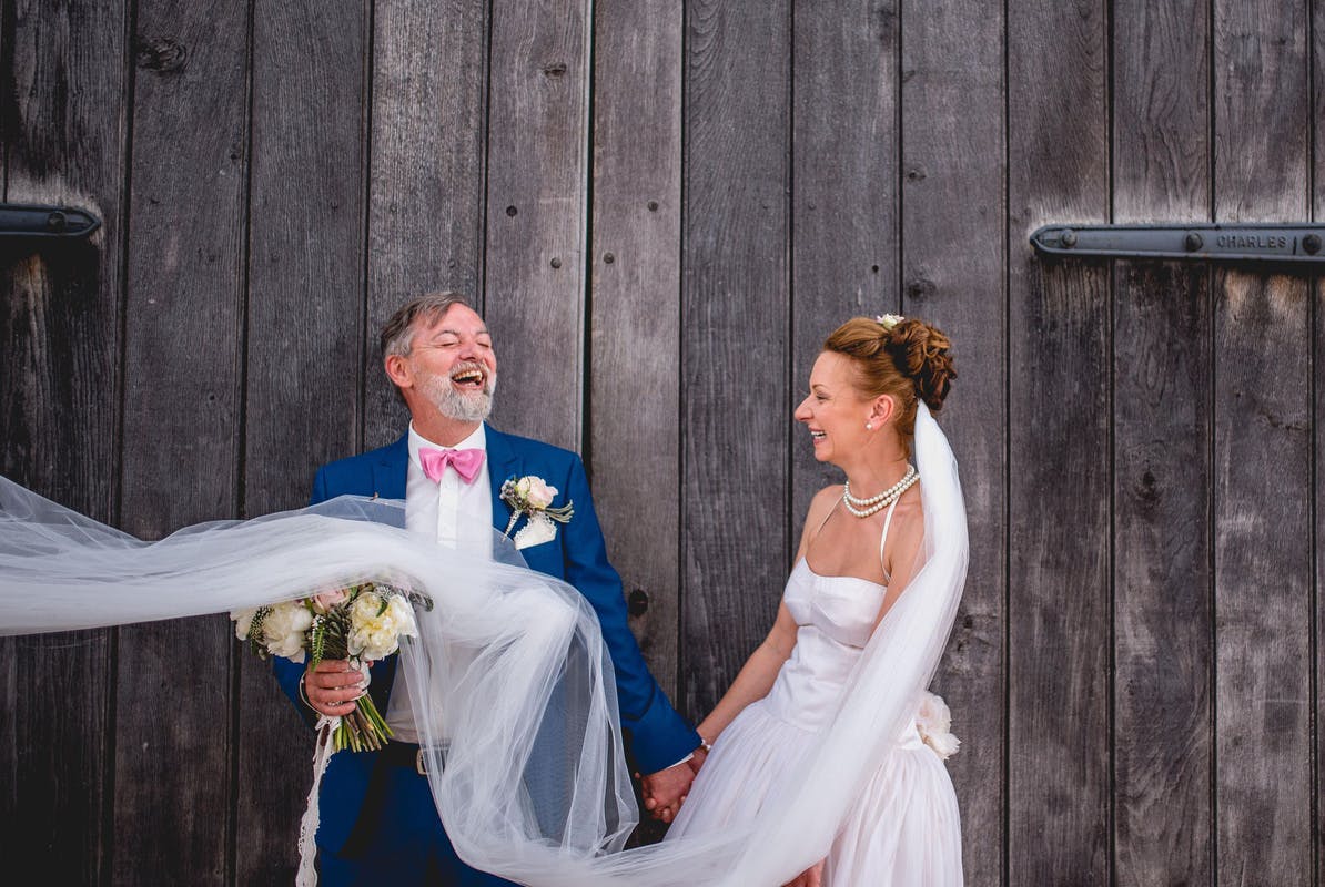 Joyful couple at Blakesley Hall barn wedding with flowing veil and rustic charm.