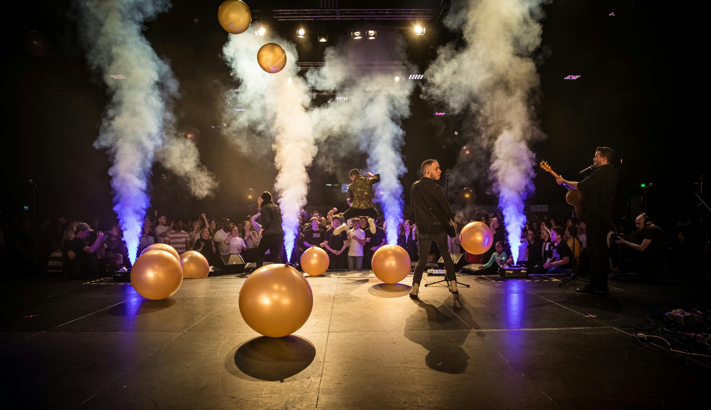 Dynamic auditorium event with performers, vibrant lighting, and engaged audience.