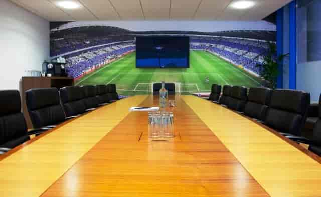 Modern conference room at Reading FC, featuring a wooden table and stadium backdrop.